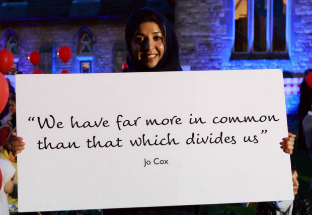 A young woman holding up a placard with the text "we have far more in common than that which divides us" - Jo Cox
